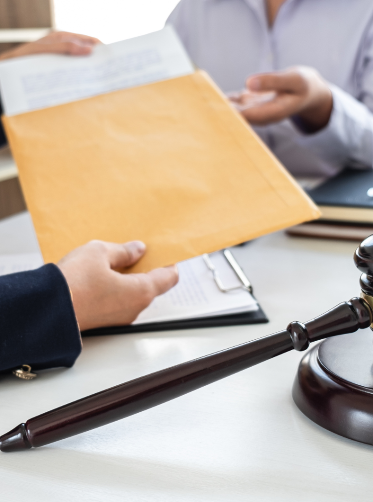 Reunión profesional con entrega de documentación legal, mazo de juez y balanza en un despacho jurídico.