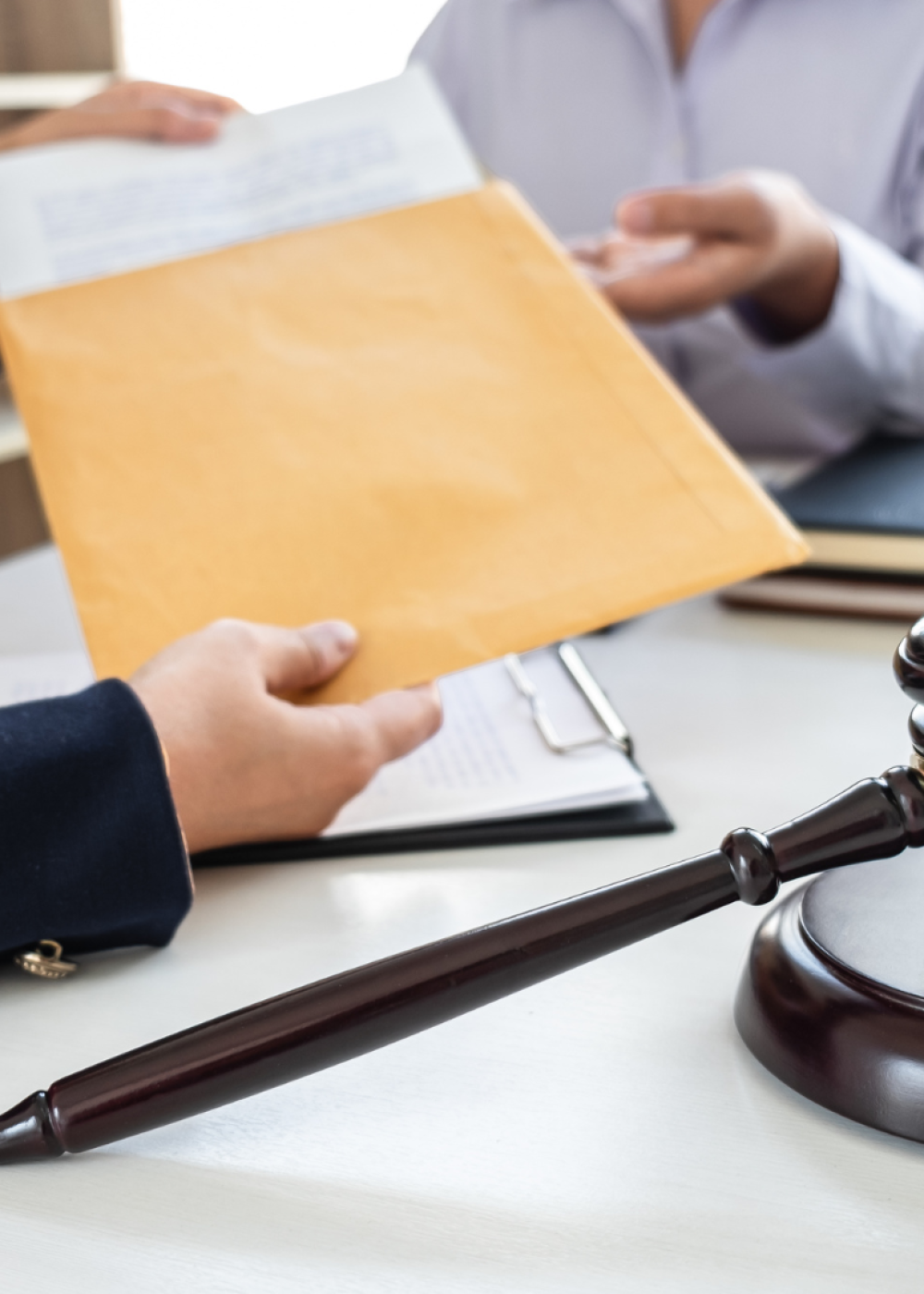Reunión profesional con entrega de documentación legal, mazo de juez y balanza en un despacho jurídico.